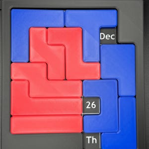 K&ouml;nnte beinhalten: Ein rotes und blaues Puzzle mit dem Datum 26. Dezember darauf. Das Puzzle ist aus Kunststoff und hat einen schwarzen Rahmen.