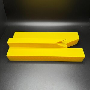 May include: A yellow plastic object with a rectangular shape and a slight bend in the middle.