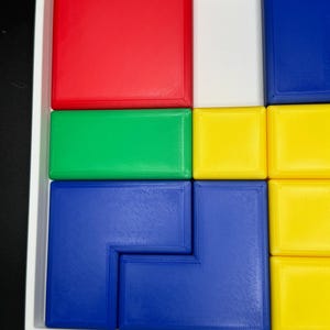 May include: A puzzle with a variety of colored blocks. The blocks are arranged in a grid pattern, with red, green, yellow, and blue blocks. The puzzle is made of plastic and has a smooth, glossy finish.