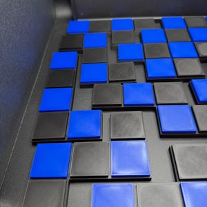 May include: A close-up of a checkerboard-like arrangement of black and blue square tiles. The tiles are arranged in a grid pattern, with alternating colors. The blue tiles are a vibrant shade, while the black tiles have a textured appearance.
