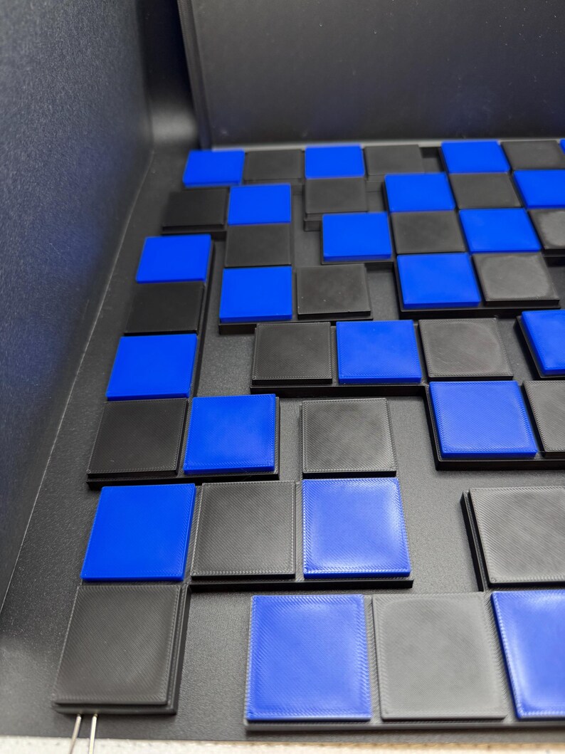 May include: A close-up of a checkerboard-like arrangement of black and blue square tiles. The tiles are arranged in a grid pattern, with alternating colors. The blue tiles are a vibrant shade, while the black tiles have a textured appearance.