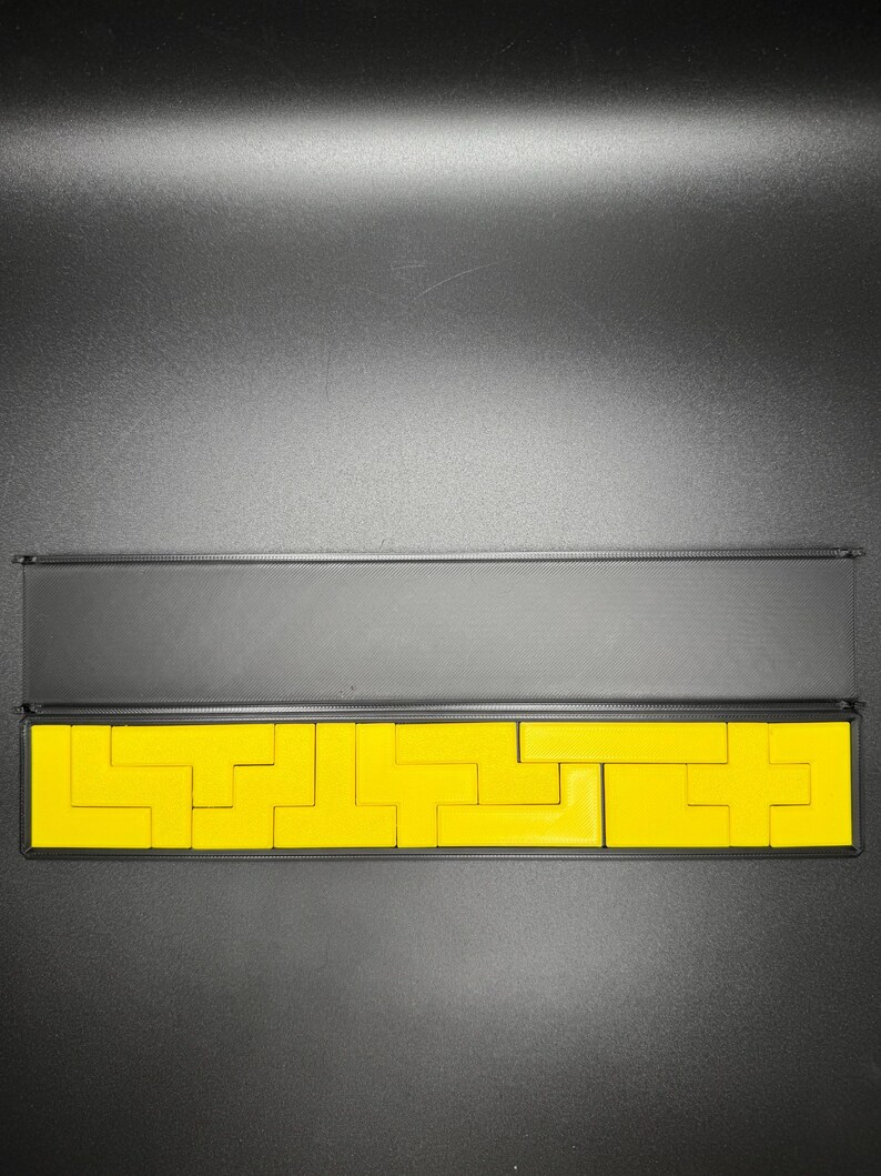 May include: A set of yellow wooden puzzle pieces in a black box. The pieces are arranged in a pattern that resembles a maze.