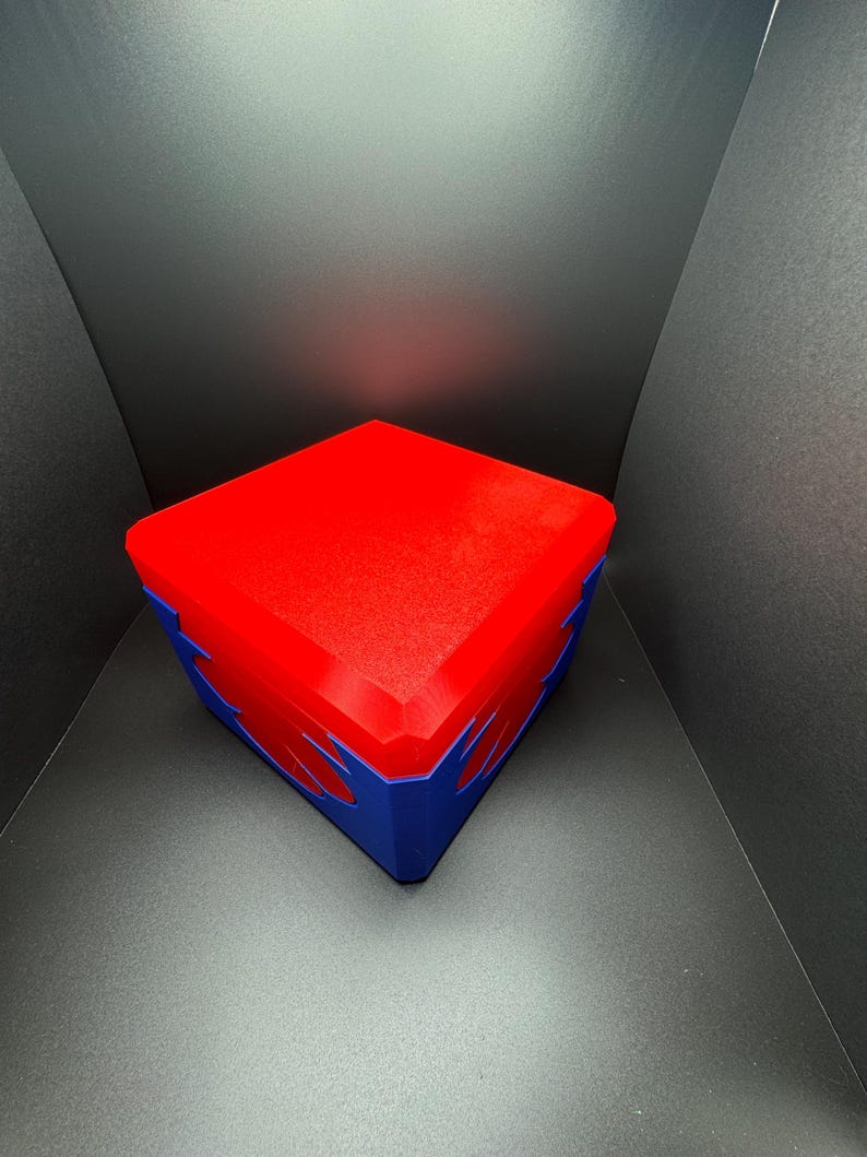 May include: A red and blue cube-shaped box with a textured surface. The box is closed and has a design on the sides.