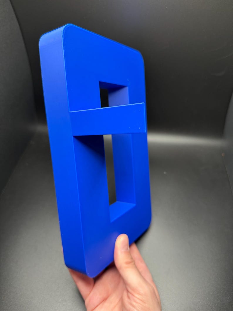 May include: A bright blue plastic letter 'B' with a hollow center. The letter is standing upright on a dark surface.