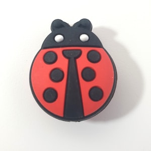 Op de afbeelding: Een rode lieveheersbeestje-bedel met zwarte stippen en een zwart hoofd. Het lieveheersbeestje heeft witte ogen.