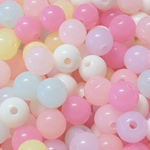 May include: A collection of pastel-coloured plastic beads. The beads are round and have a hole in the centre. The colours include pink, yellow, blue, and purple.