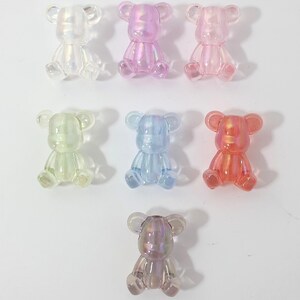 May include: Seven iridescent plastic bear figurines in various pastel colors, including pink, blue, green, and purple. The bears are sitting with their paws outstretched.