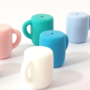 Op de afbeelding: Zeven kleurrijke siliconen bekers met een handvat. De bekers zijn in de kleuren bruin, roze, wit, blauw, turquoise, lichtblauw en roze.
