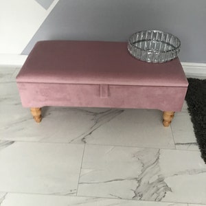 May include: A dusty pink velvet storage bench with wooden legs and a decorative silver bowl on top.