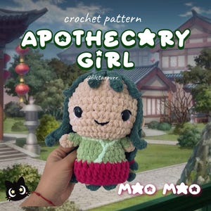 May include: A handmade crochet doll with the text "APOTHECARY GIRL". The doll has a light brown face, green hair, a green and red outfit, and black eyes. The doll is held in a hand.