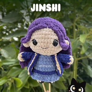 Pode incluir: Boneca de crochê feita à mão com peruca roxa, jaqueta azul e pele clara. A boneca tem olhos grandes e pretos e um rosto sorridente. O texto na imagem diz "crochet pattern release JINSHI" e "Lilstarpurr".