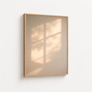 以下が含まれることがあります： 長方形の額装されたアートワーク。薄茶色のマットが付いています。フレームは明るい木の色です。アートワークは白い壁に取り付けられています。窓の影がアートワークに映っています。