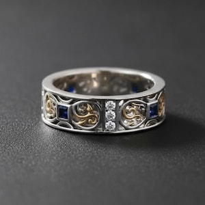 以下が含まれることがあります： 黒い持ち手と「But First, Coffee」のテキストが太字の黒で書かれた白いセラミックマグ。マグカップはぼやけた背景に置かれており、居心地の良い環境を示唆しています。