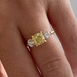 May include: A gold ring with a large, square-cut yellow diamond in the center and two smaller round diamonds on either side.