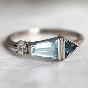 May include: A silver ring with a triangular aquamarine gemstone, a smaller round diamond, and a smaller triangular blue topaz gemstone.