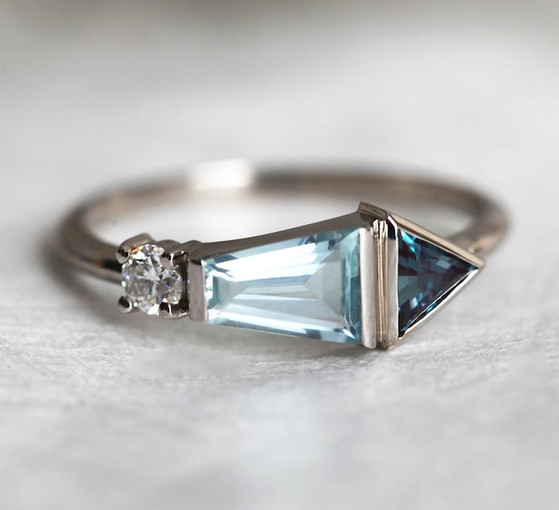 May include: A silver ring with a triangular aquamarine gemstone, a smaller round diamond, and a smaller triangular blue topaz gemstone.