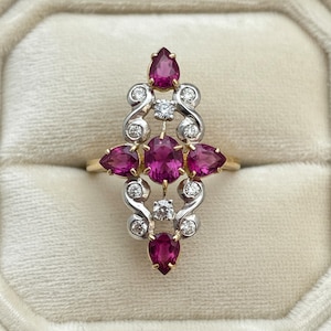 May include: A vintage-style ring featuring a cluster of vibrant, oval and pear-shaped ruby gemstones. The ring has a gold band and a silver-tone setting with small, round diamonds. The design is symmetrical and ornate, with a classic, elegant aesthetic.