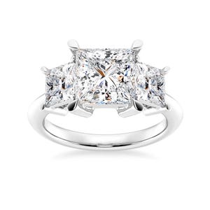 May include: A three-stone engagement ring with a large square-shaped center diamond and two smaller square-shaped diamonds on either side.