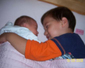 Op de afbeelding: Een jong kind met bruin haar houdt een jonger kind vast met een wit deken. Het oudere kind draagt een blauw en oranje shirt. Het jongere kind draagt een wit shirt. De afbeelding is gedateerd 18/09/2008.