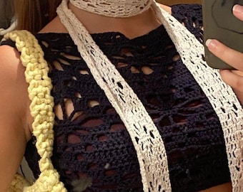 Peut inclure: Un collier ras de cou en crochet blanc avec une longue écharpe en crochet blanc. L'écharpe est drapé sur un haut en crochet noir.