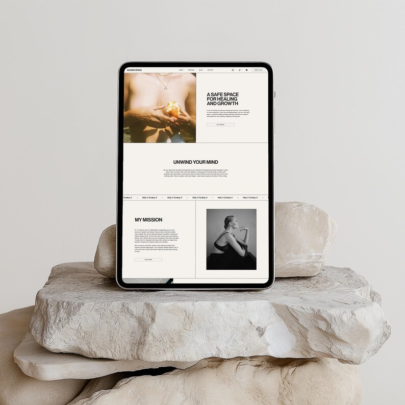 May include: A tablet displaying a website with the text "A Safe Space for Healing and Growth" and "Unwind Your Mind." The tablet rests on a stack of light-colored, textured stones. The website features images and text.
