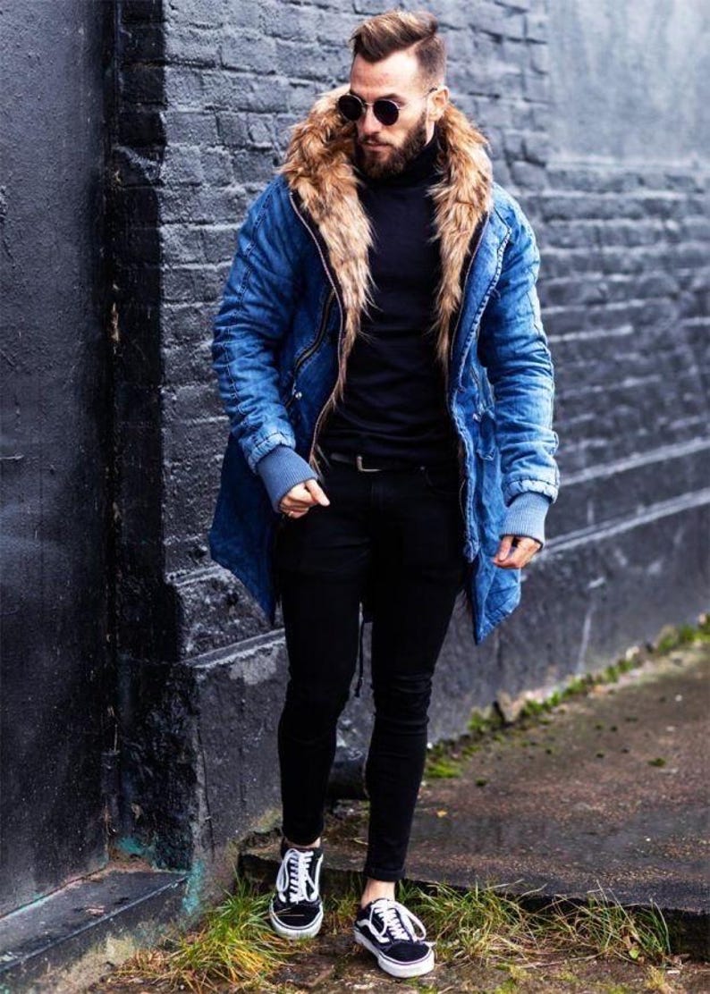 May include: A blue denim parka with a large tan faux fur hood lining, a black turtleneck sweater, black slim-fit trousers, and black and white low-top sneakers. The jacket features ribbed gray cuffs and a front zipper closure.