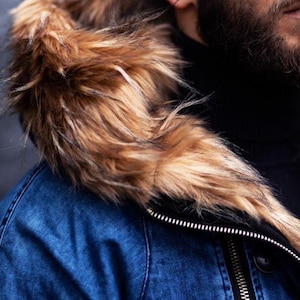 May include: A blue denim jacket featuring a large hood trimmed with thick, textured faux fur in shades of brown, tan, and black. The jacket includes a prominent silver-toned metal zipper running vertically along the front closure.