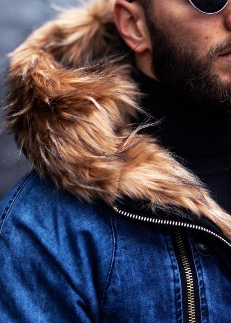 May include: A blue denim jacket featuring a large hood trimmed with thick, textured faux fur in shades of brown, tan, and black. The jacket includes a prominent silver-toned metal zipper running vertically along the front closure.