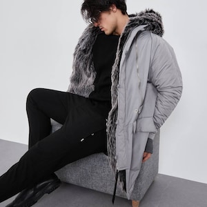 May include: A light gray parka featuring a hood lined with dark gray and white faux fur, a front zipper closure, and long sleeves with ribbed cuffs. The coat is worn over a black long-sleeved sweater and black trousers with black leather shoes.