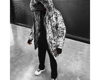 May include: A long parka jacket featuring a black and white abstract graphic print, a large hood lined with thick grey and black faux fur, a front zipper closure, and long sleeves with black fingerless glove cuffs, worn over a black shirt and pants.