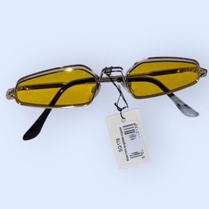 May include: Gold-rimmed sunglasses with yellow lenses. The sunglasses have a tag attached that reads "SG178 metal sunglasses frame size 52mm".