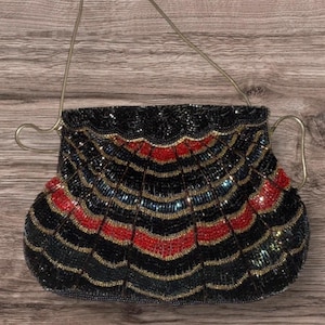 Può includere: Una borsetta vintage con perline e un design a ventaglio. La borsa presenta uno sfondo nero con accenti rossi e dorati. Ha un manico argentato e una forma strutturata, ideale per serate o occasioni speciali.