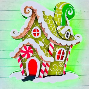 May include: A decorative gingerbread house, featuring a green exterior with white accents, red windows and door, and candy cane stripes. The roof is covered in white frosting and snow. A large peppermint candy is on the front. The house is layered.