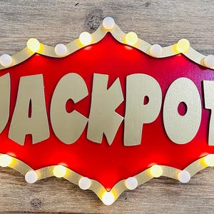 May include: A red and gold sign with the word "JACKPOT" in gold letters. The sign has a border of white lights.