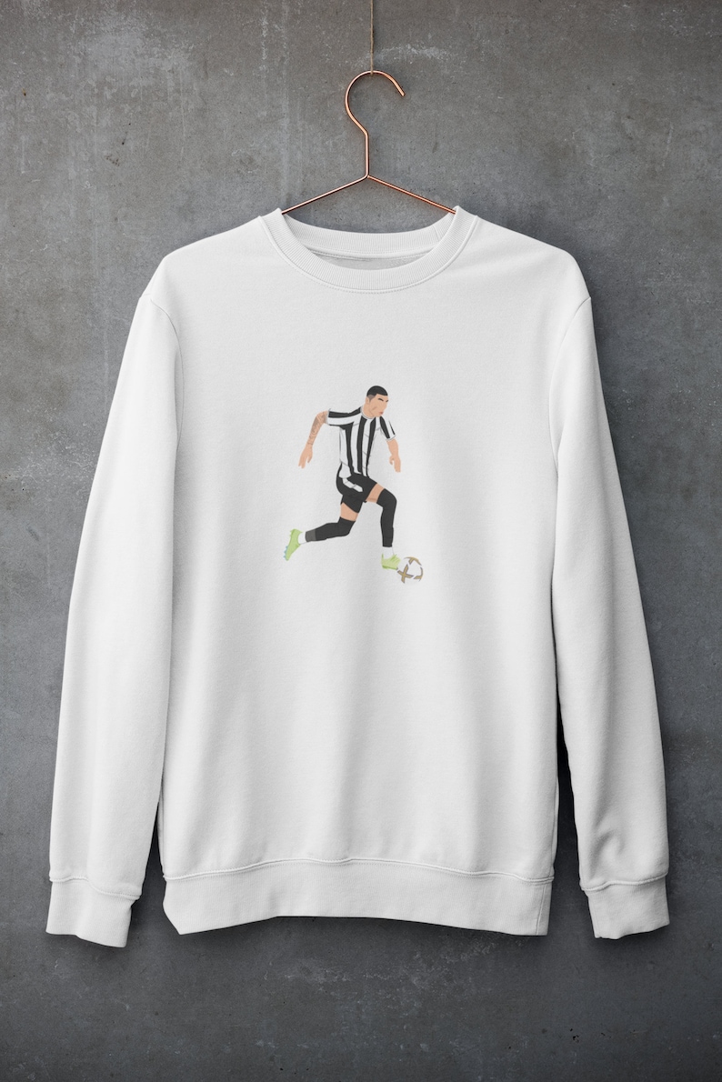 Puede incluir: Sudadera blanca con una ilustraci&oacute;n en blanco y negro de un jugador de f&uacute;tbol driblando el bal&oacute;n.