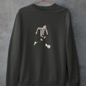 Puede incluir: Una sudadera gris oscuro con una ilustraci&oacute;n en blanco y negro de un jugador de f&uacute;tbol que dribla el bal&oacute;n.