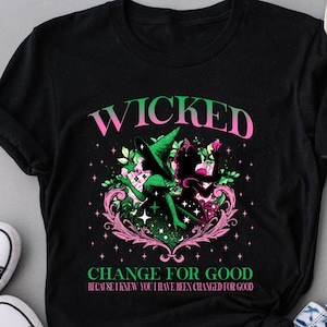 May include: Black t-shirt featuring the word "WICKED" in pink, with a green and pink graphic of two figures. The text "CHANGE FOR GOOD" is below the graphic. Black Converse trainers and blue jeans are also in the image.