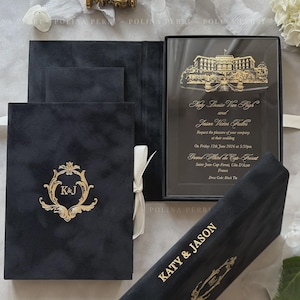 May include: A black velvet wedding invitation box set featuring gold foil lettering and a gold crest with the initials K&J. The set includes a clear acrylic invitation card with a gold illustration of a hotel and the text Katy Louise Van Pagh and Jason Victor Fuller.
