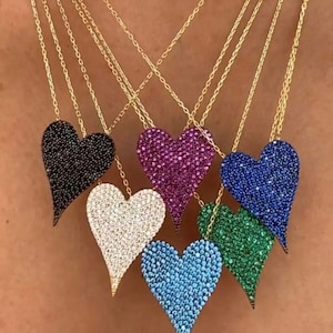 Puede incluir: Seis collares de oro con colgantes en forma de corazón. Los colgantes están cubiertos de pequeñas piedras brillantes y vienen en negro, blanco, rosa, azul, verde y azul claro.
