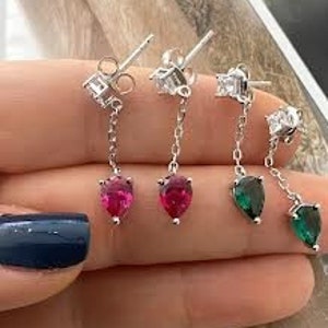 Könnte beinhalten: Ein Paar silberne Ohrhänger mit tropfenförmigen roten und grünen Edelsteinen. Die Ohrringe haben ein schlichtes Design und sind perfekt für den Alltag.