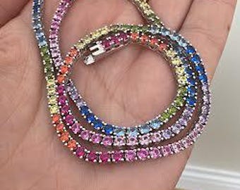Könnte beinhalten: Eine silberne Halskette mit einem Regenbogen aus farbigen Edelsteinen. Die Halskette wird in einer Hand gehalten, wodurch die lebendige Anordnung von rosa, blauen, orangefarbenen, gelben und grünen Steinen hervorgehoben wird. Der Verschluss ist sichtbar.