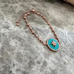 Pu&ograve; includere: Un braccialetto regolabile in oro rosa con un ciondolo turchese con un design a stella. Il ciondolo &egrave; decorato con strass trasparenti.