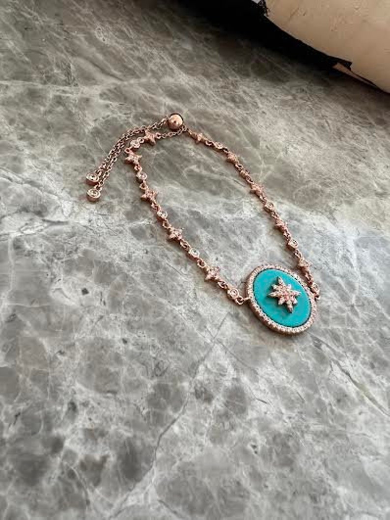 Pu&ograve; includere: Un braccialetto regolabile in oro rosa con un ciondolo turchese con un design a stella. Il ciondolo &egrave; decorato con strass trasparenti.