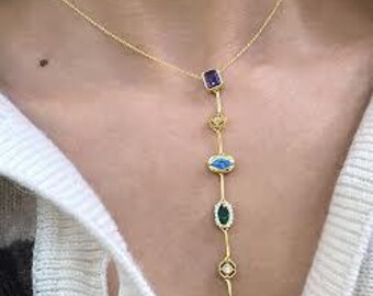 May include: A gold chain necklace with a variety of colorful gemstones. The necklace features a long, dangling design with a purple, blue, green, and pink stone.