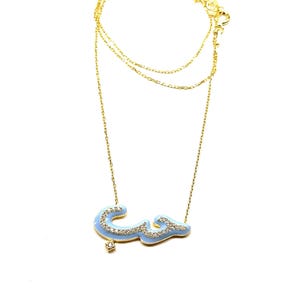 May include: A gold chain necklace with a light blue pendant featuring the Arabic word for "love" in sparkling diamonds.