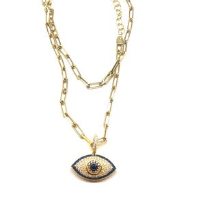 May include: Gold chain necklace with a blue and white evil eye pendant. The pendant is covered in small white stones and has a blue center.