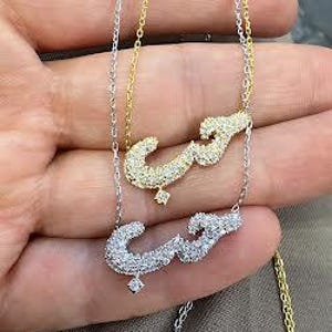 May include: Two delicate necklaces with a pendant in the shape of the Arabic word for love, set with sparkling cubic zirconia stones. One necklace is silver and the other is gold.
