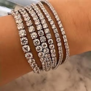 Può includere: Un set di braccialetti da tennis in argento con pietre di zircone cubico trasparenti.