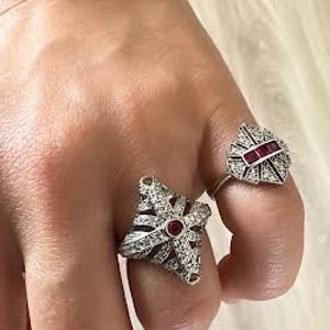 May include: Two silver rings with red gemstones. The ring on the left is a starburst design and the ring on the right is a heart shape.