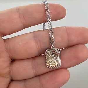 May include: A silver chain necklace with a silver pendant featuring a sunburst design with small clear stones.